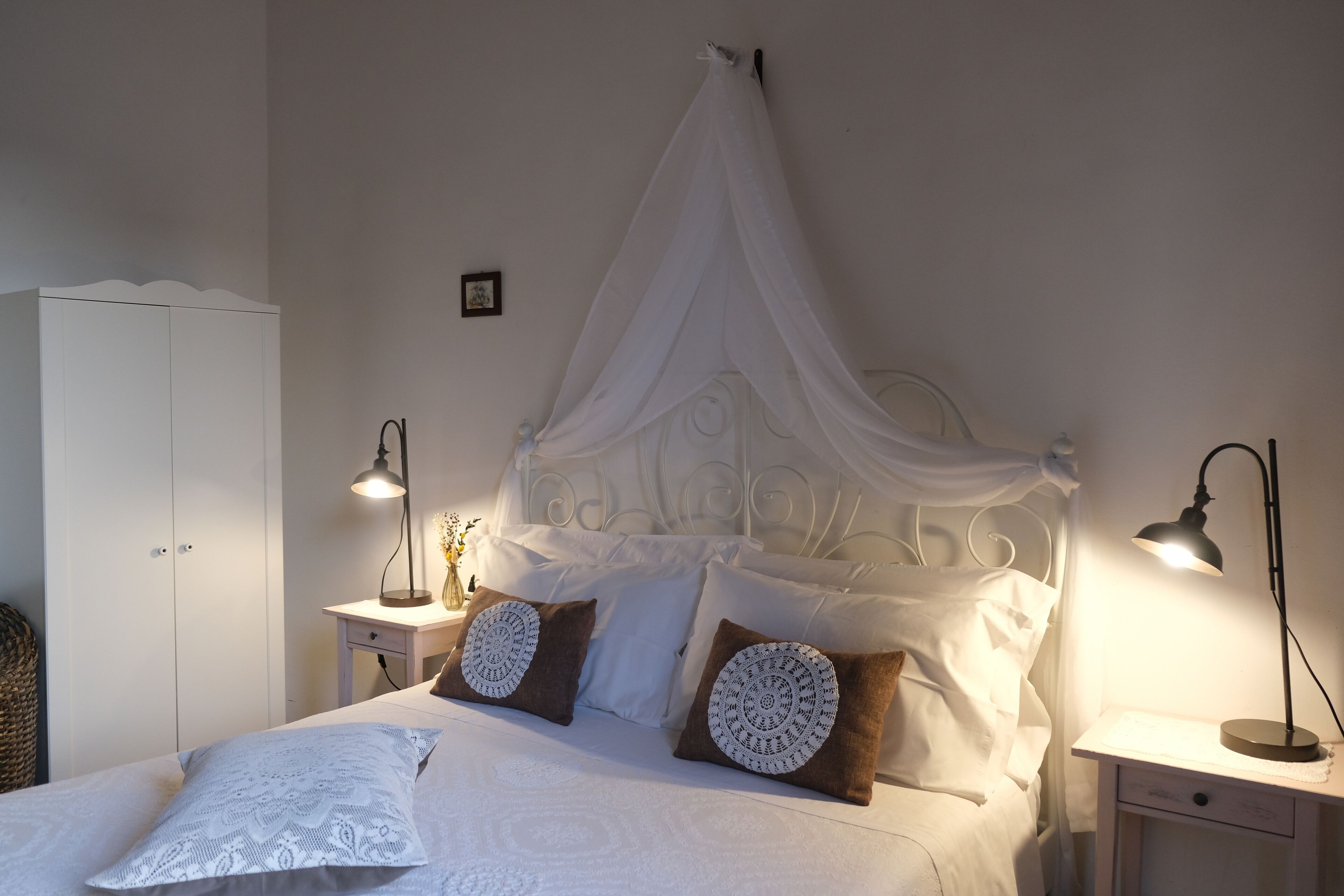 Una cama bien hecha con dosel, dos lámparas de noche y una mesita de noche con lámpara.