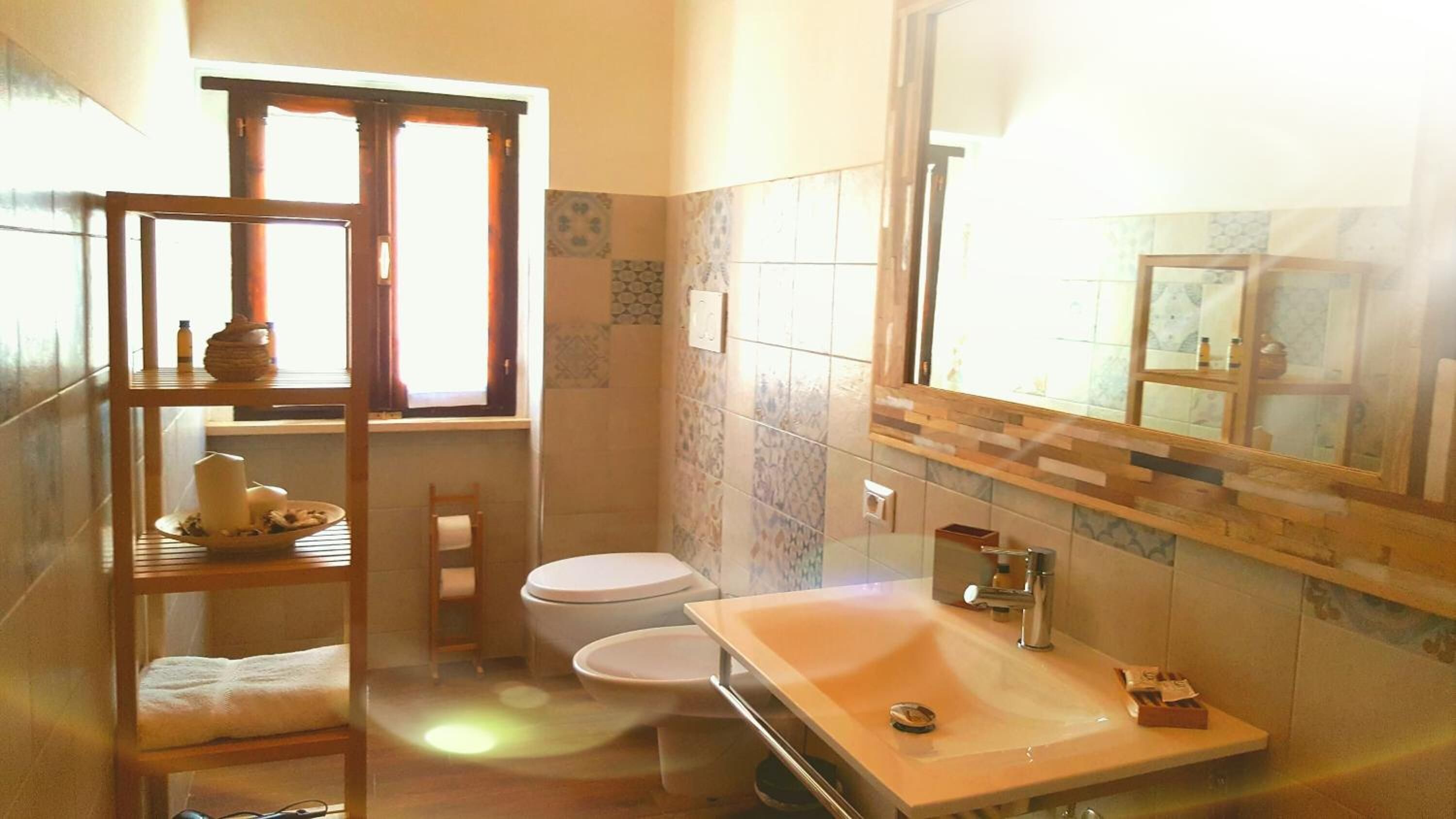 A bathroom with a wooden shelf, two toilets, a sink, and a mirror.