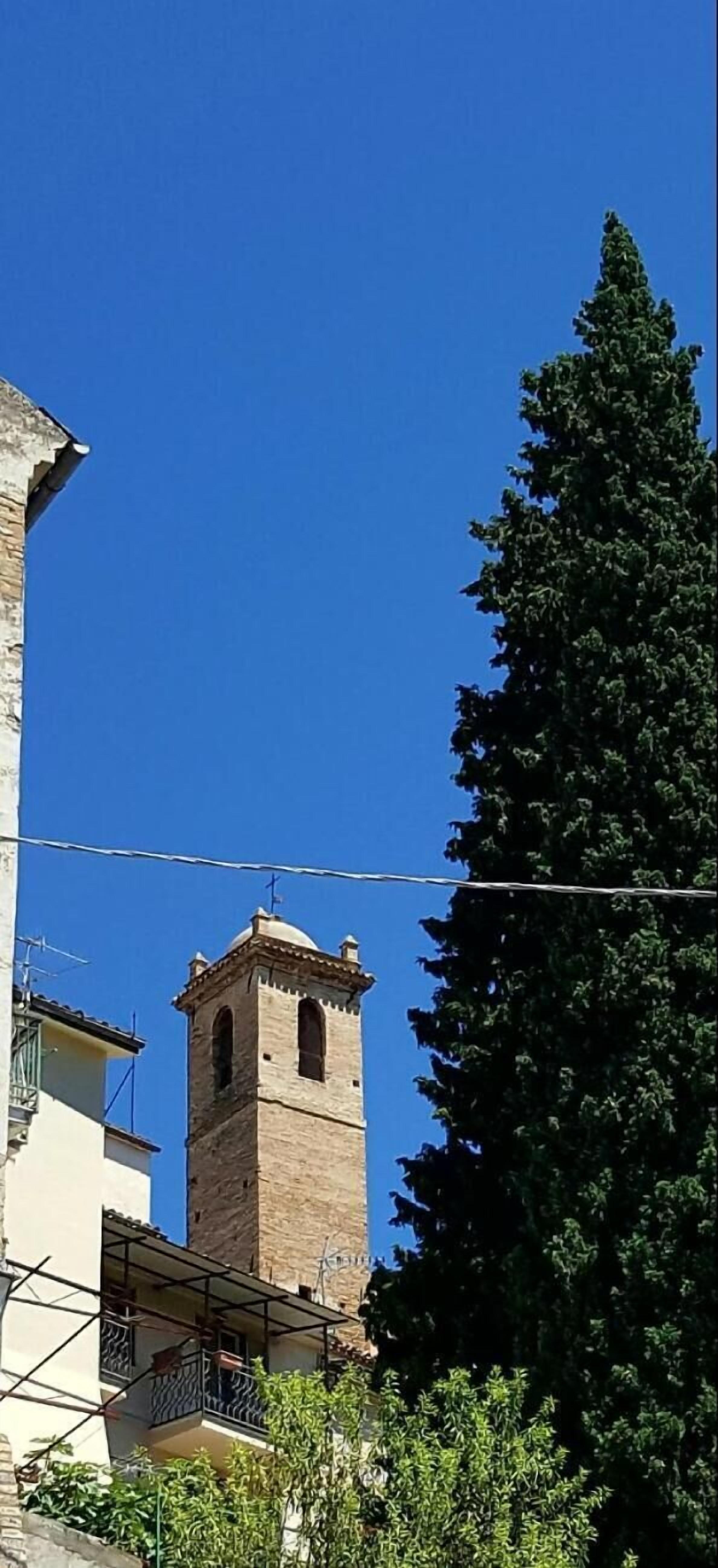 Una torre con una campana, un cielo azul despejado y un árbol grande.