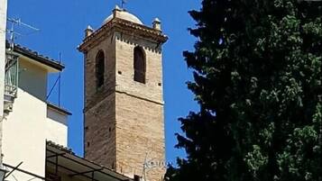 Una torre con una campana, un cielo azul despejado y un árbol grande.
