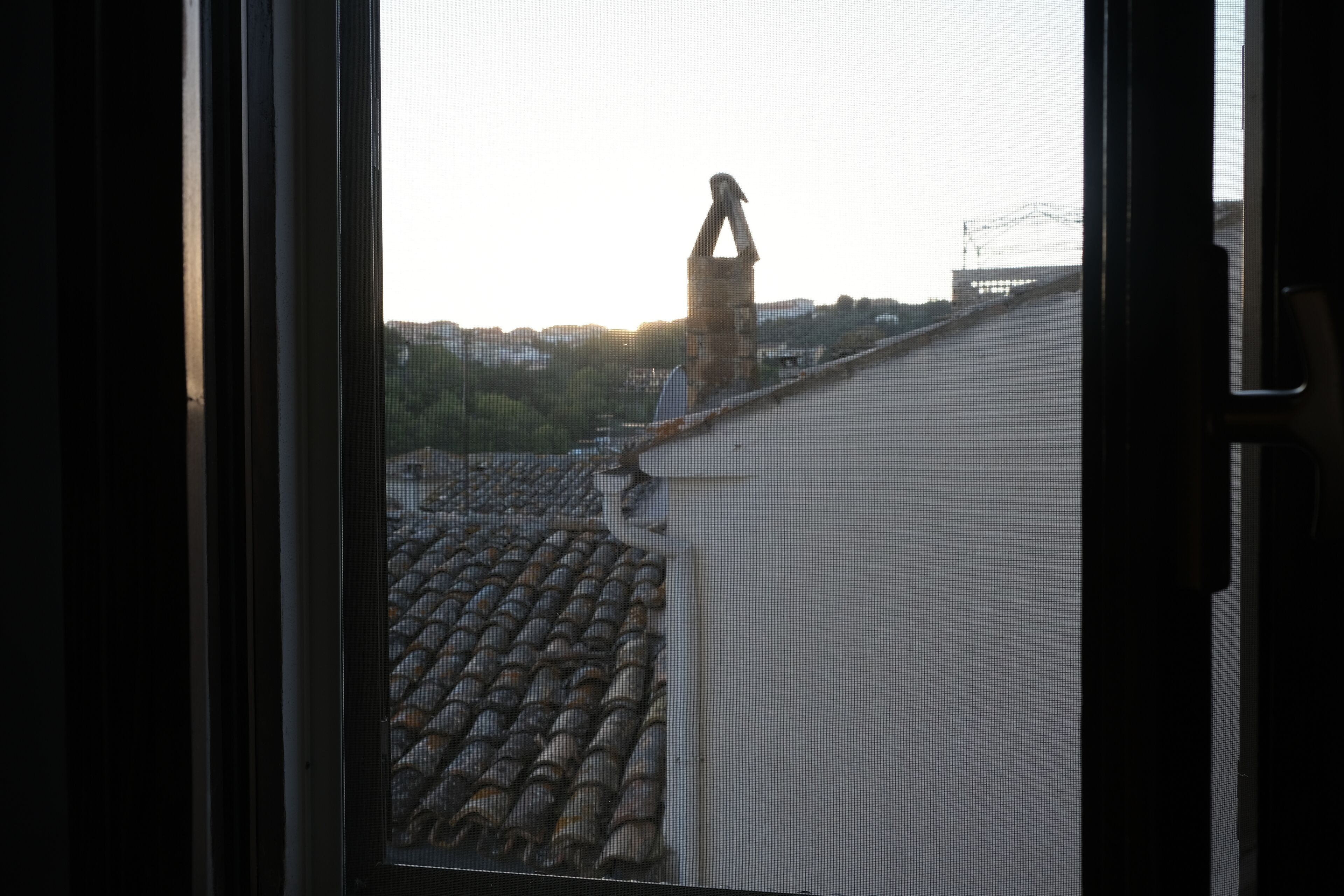 A view through a window of a building with a tiled roof and a chimney.