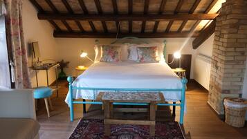 Un dormitorio con estructura de cama de madera, un banco a juego, una alfombra estampada y una pared de ladrillo.