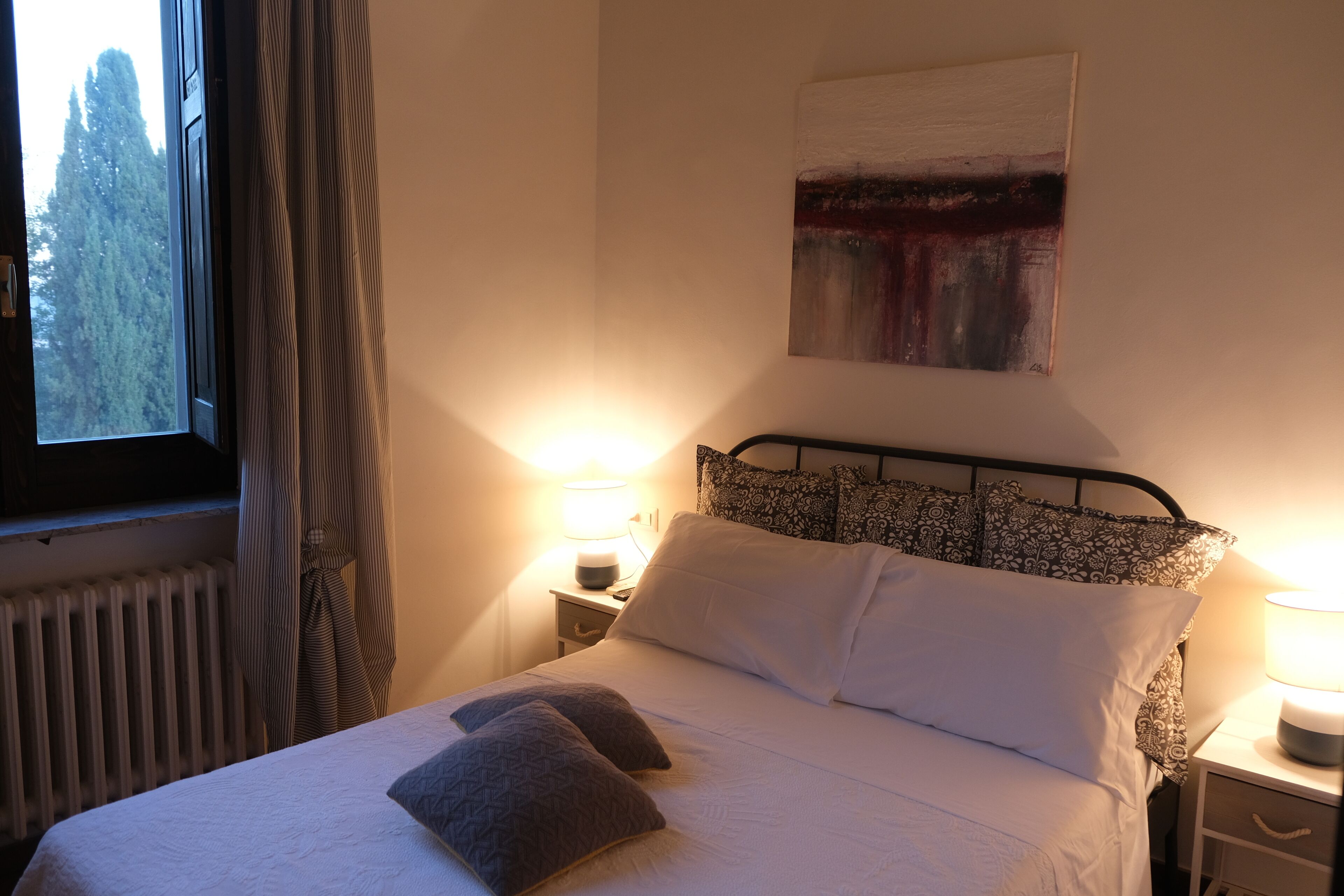 A neatly made bed with pillows, a bedside lamp, and a window with curtains.