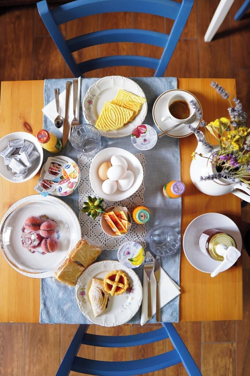A breakfast table with various food items, utensils, and a cup of coffee.