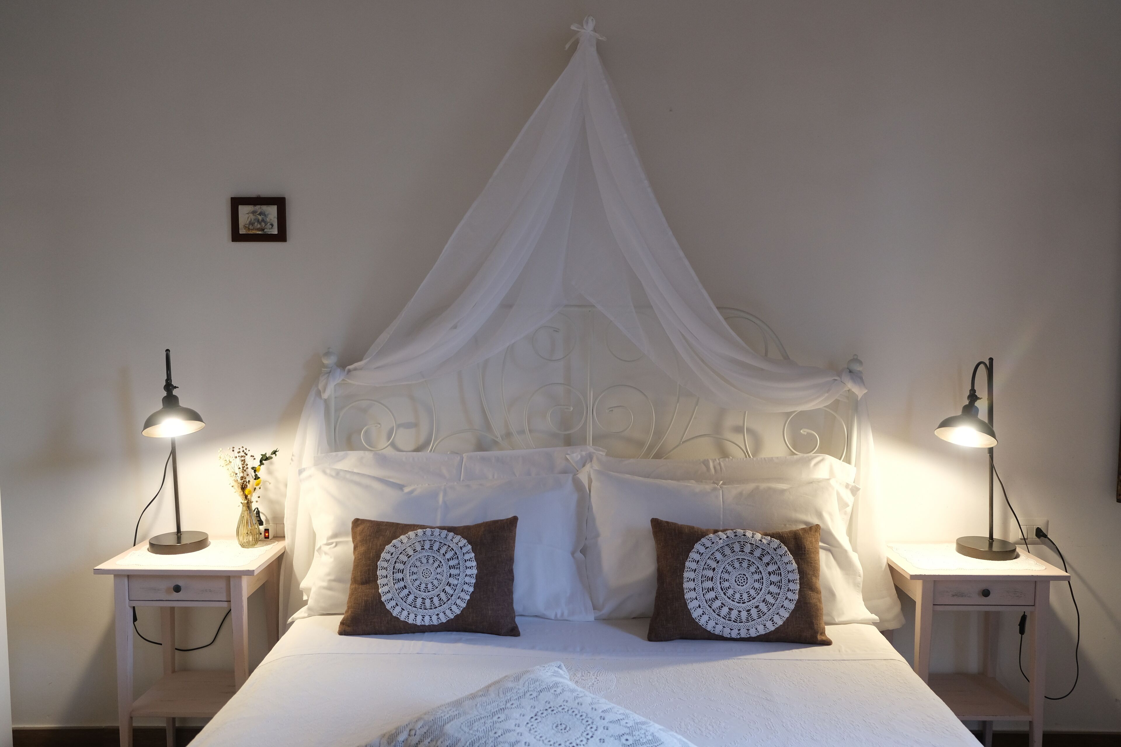 Una cama bien hecha con dosel, dos lámparas de noche y almohadones decorativos.