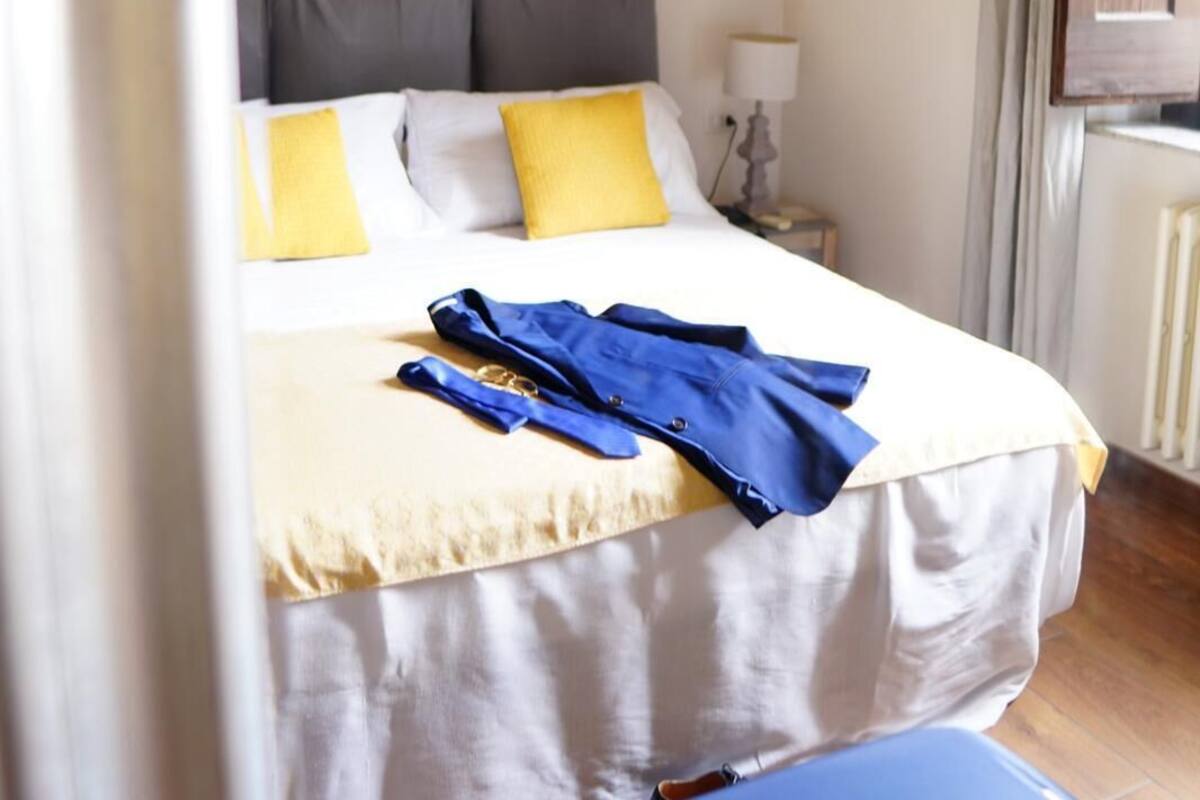 A hotel room with a bed, a bedside table, a lamp, and a window with curtains.