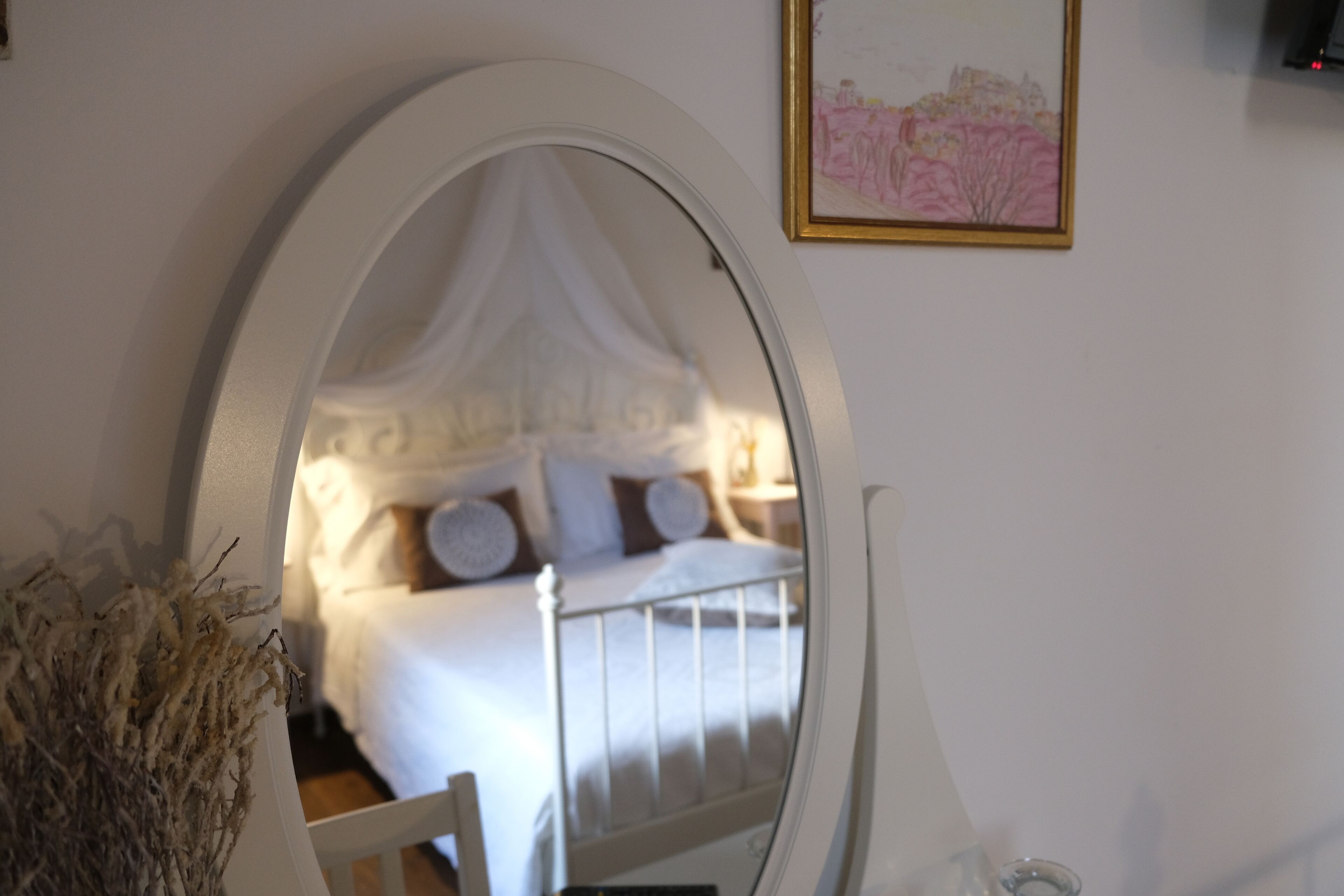 Un dormitorio con una cama con dosel blanco, una mesita de noche y un cuadro en la pared.