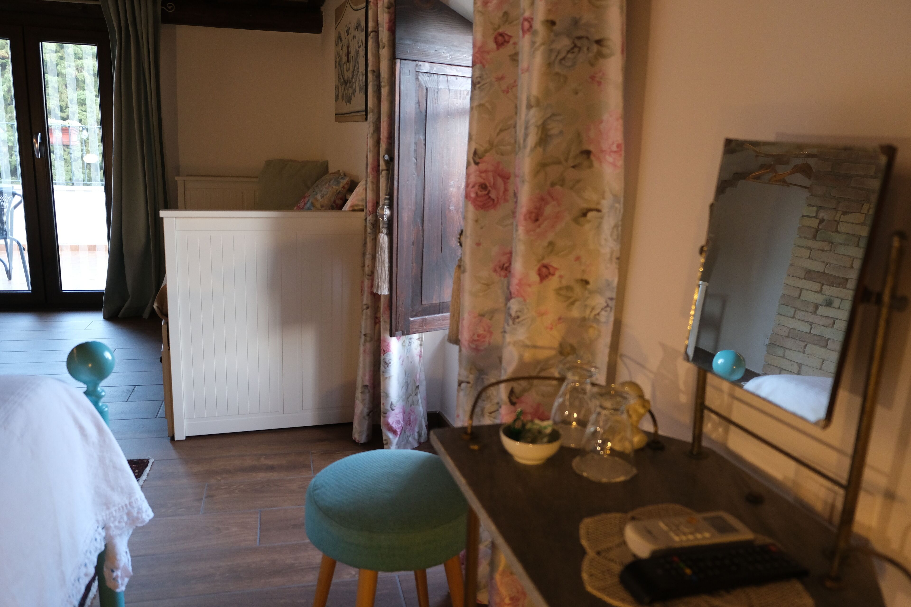 Una habitación con una cama, un escritorio con computadora, un espejo y una ventana con cortinas.