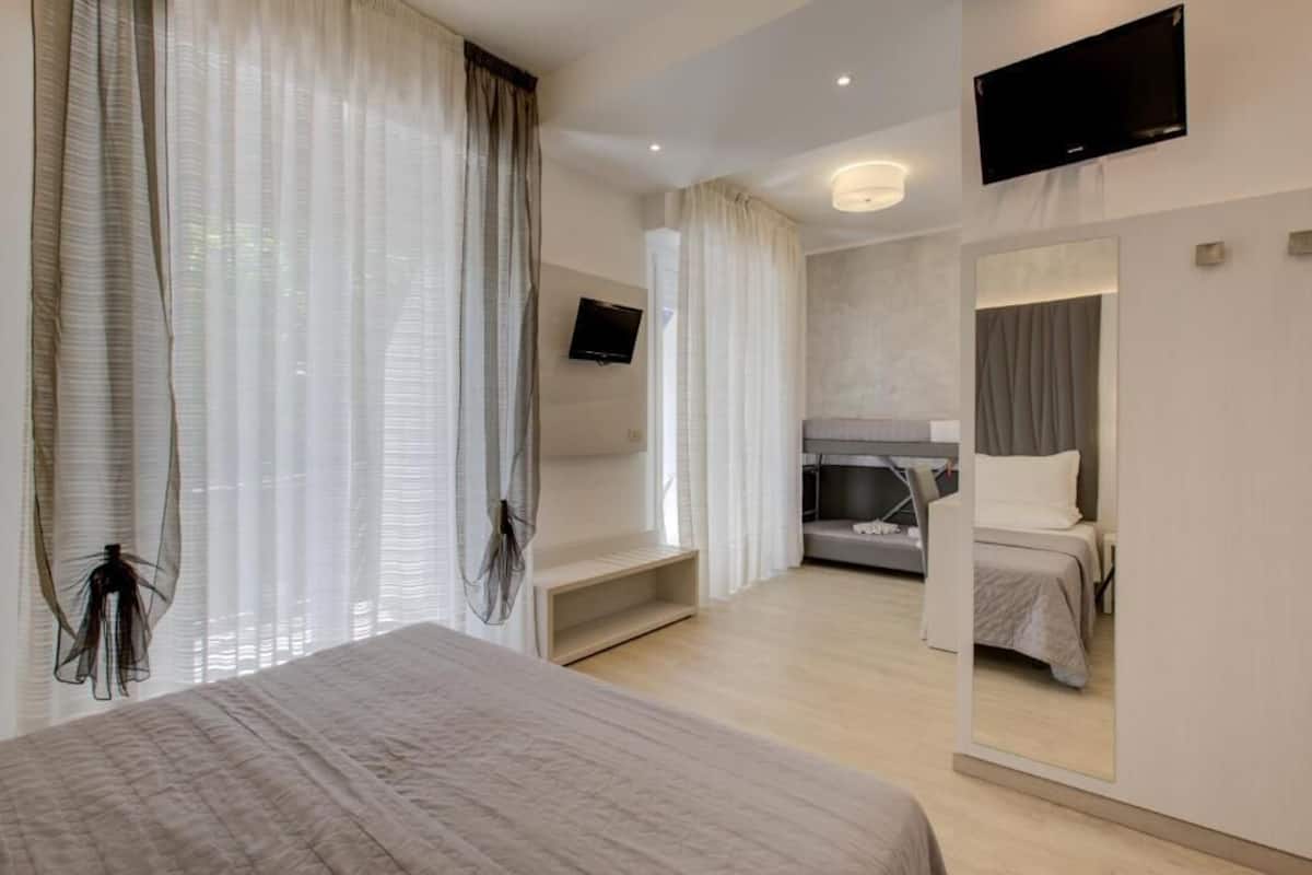 A modern hotel room with a bed, a TV, a mirror, and a seating area.