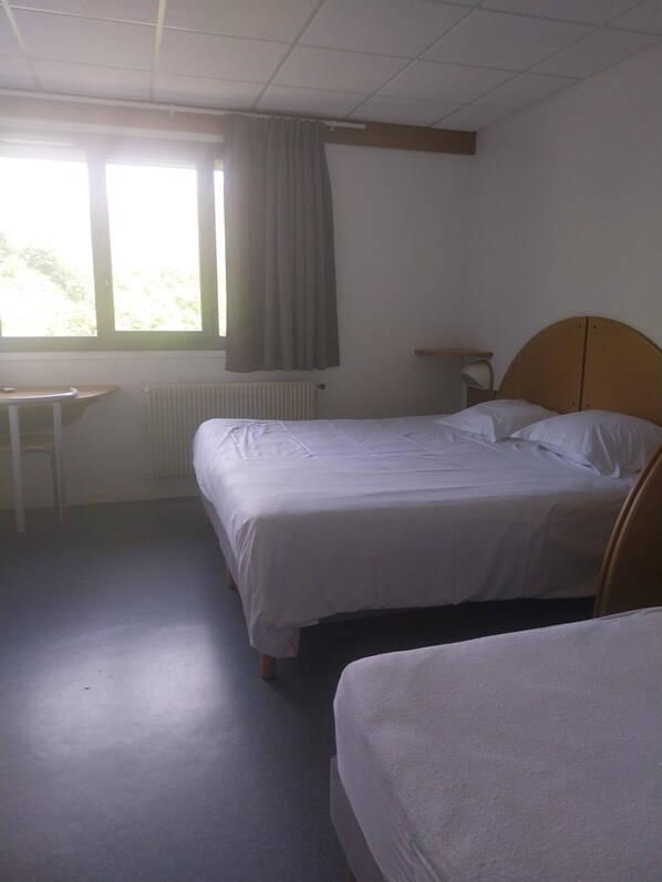 A room with two single beds, a small table, and a window with curtains.