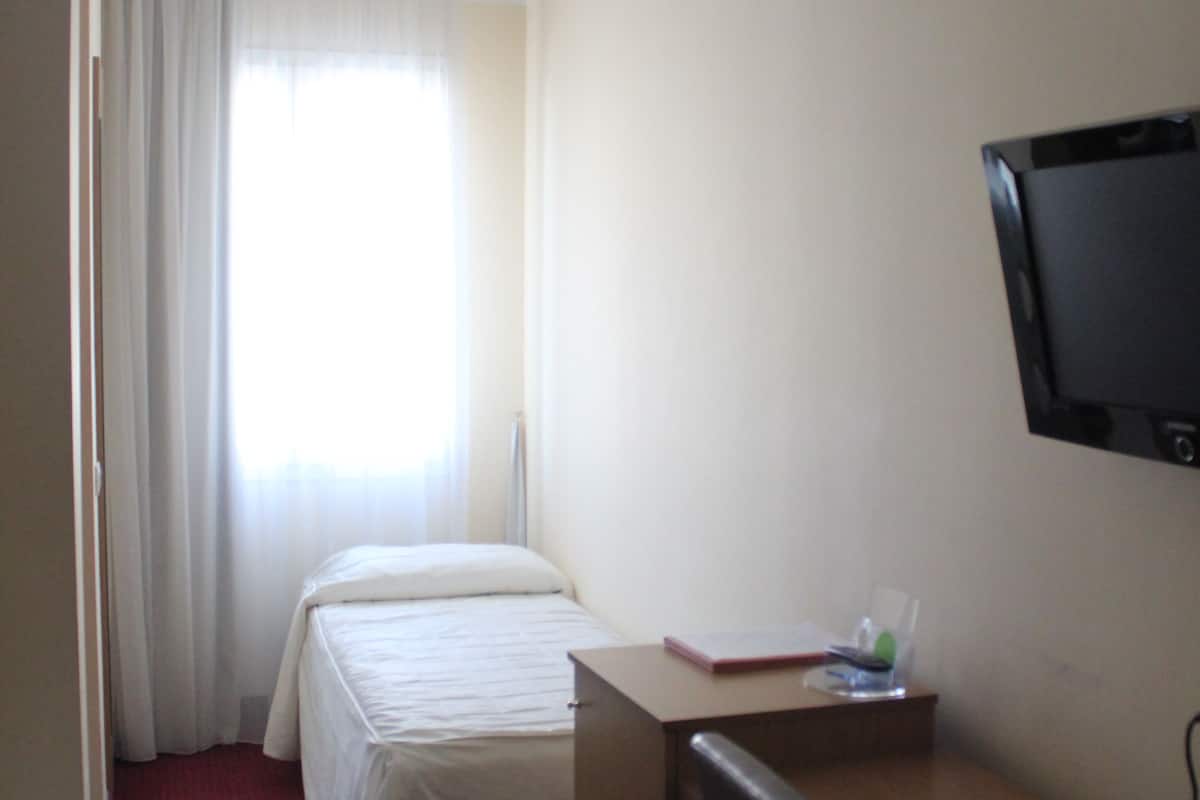 Ein Hotelzimmer mit zwei Betten, einem Schreibtisch, einem Stuhl, einem Fernseher und einem Fenster mit Vorhängen.