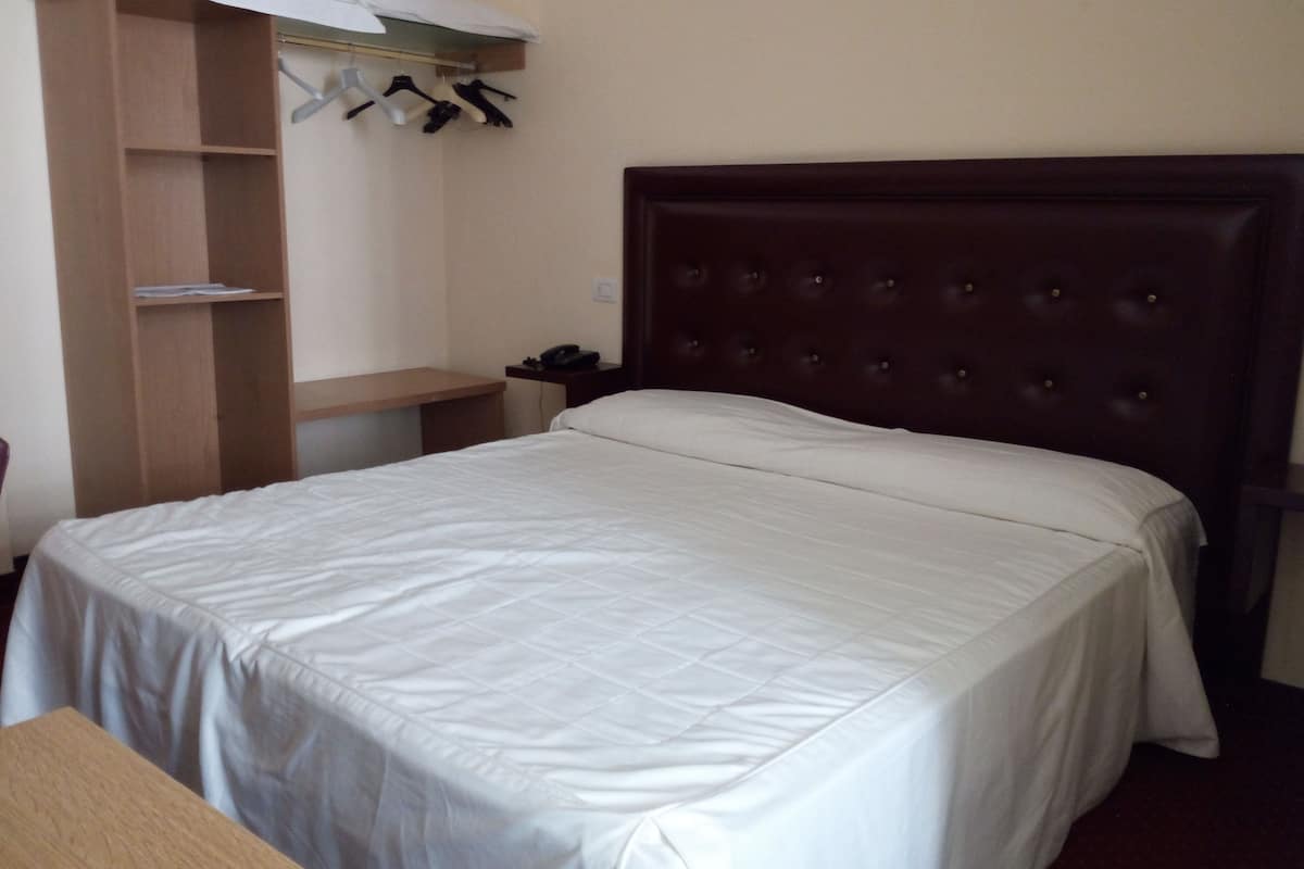 Ein Hotelzimmer mit einem großen Bett, einem Holzschrank, einem Schreibtisch und einem Kleiderhaken.