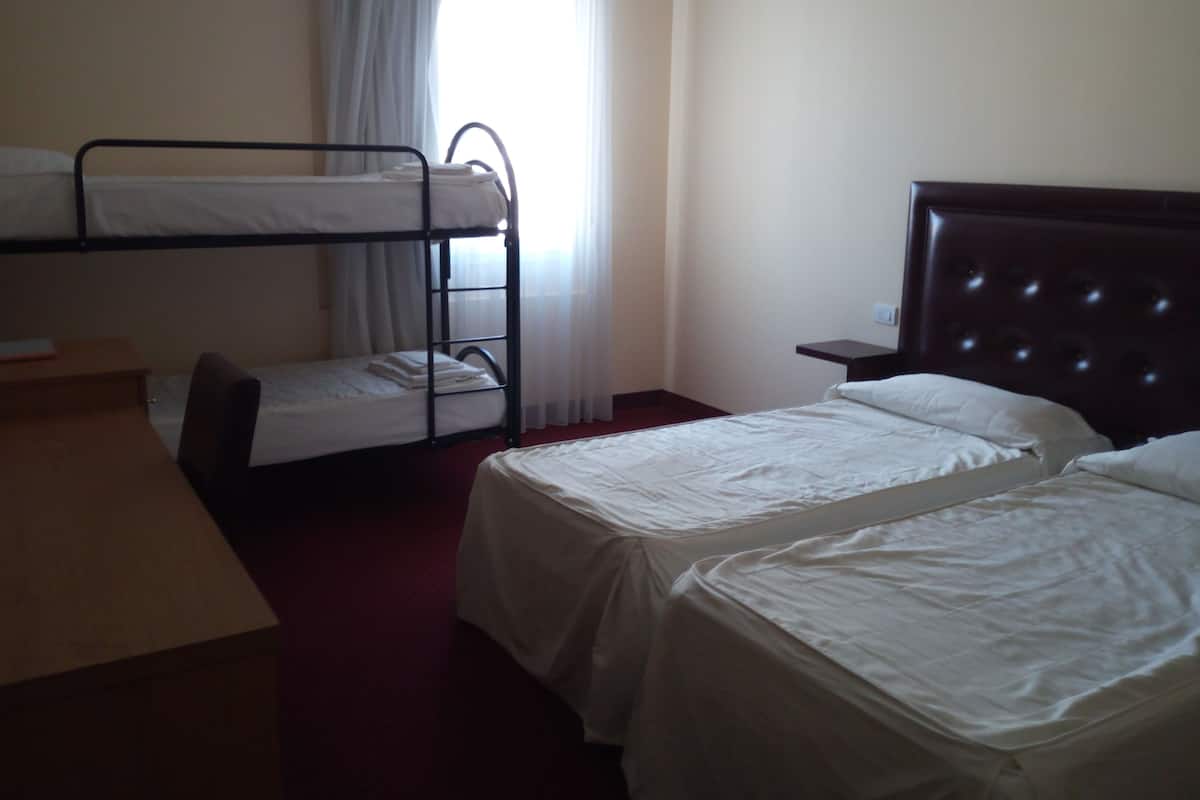 Ein Hotelzimmer mit zwei Einzelbetten, einem Stockbett, einem Schreibtisch und einem Stuhl.