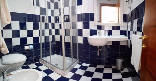 A bathroom with a checkered floor, a glass-enclosed shower, a white sink, and a toilet.