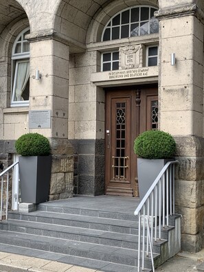 A stone building with a wooden door, two potted plants, and a sign indicating the building's historical significance.