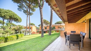 A patio with a table and chairs, surrounded by a well-maintained lawn and tall trees. - Casas Golf Relax (Pals)