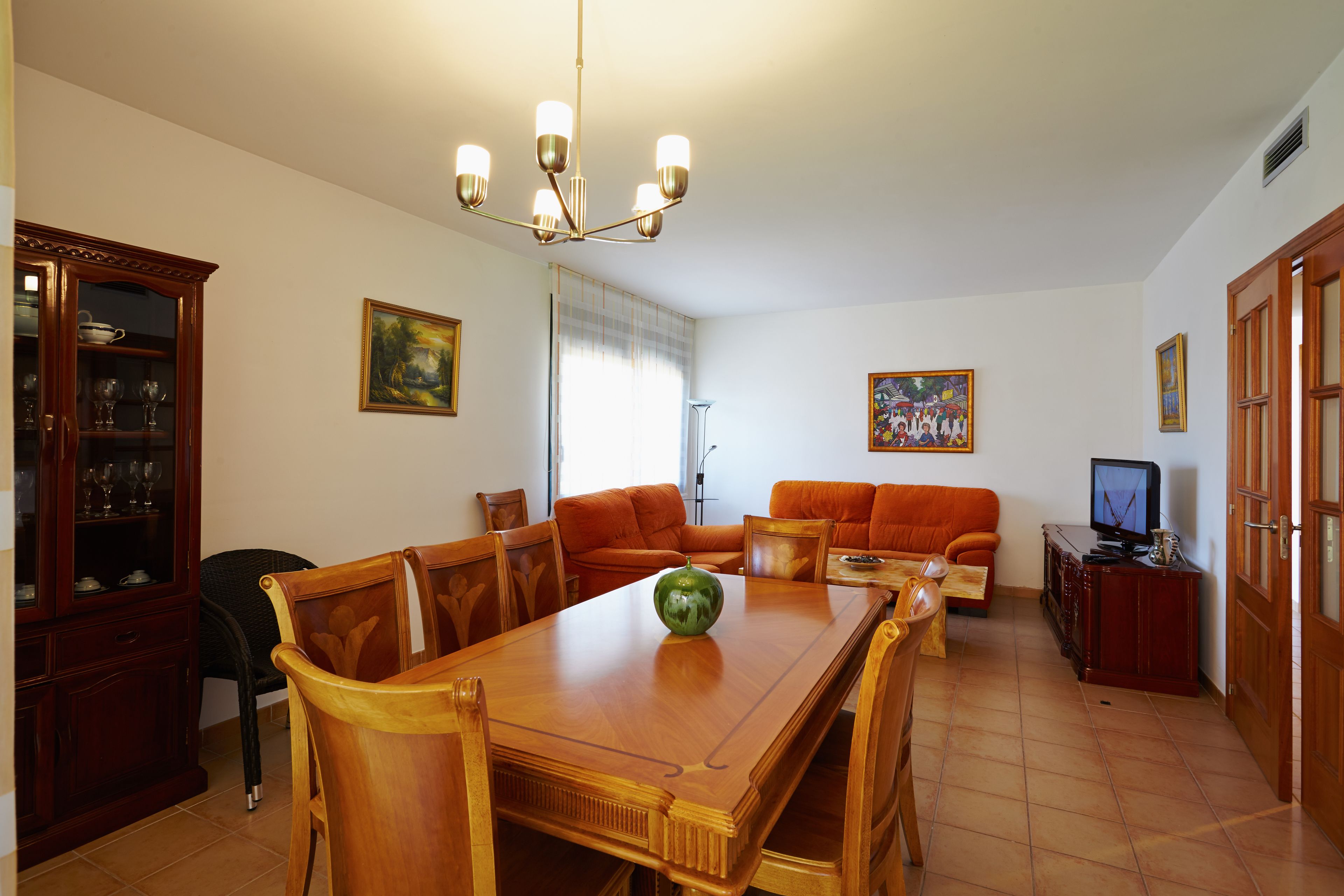 Un comedor con una mesa de madera, sillas, una araña, un sofá y una televisión.