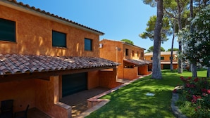 A row of stucco buildings with tiled roofs, a well-maintained lawn, and trees. - Casas Golf Relax (Pals)