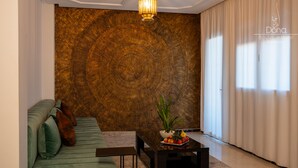 Un salon moderne avec un mur texturé, un canapé, une table basse avec des fruits et une grande fenêtre avec des rideaux.