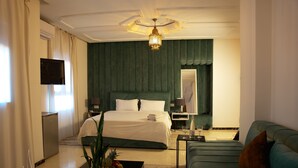 Une chambre d’hôtel avec un lit, un canapé, une télévision, un minibar et une plante.