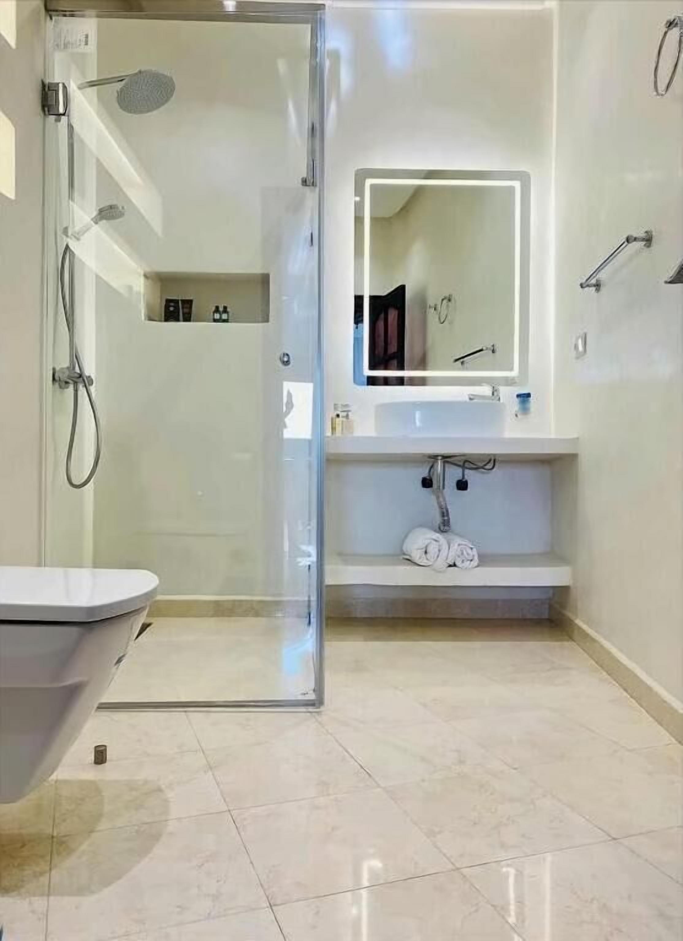Un baño moderno con cabina de ducha de vidrio, lavabo blanco con espejo y retrete.