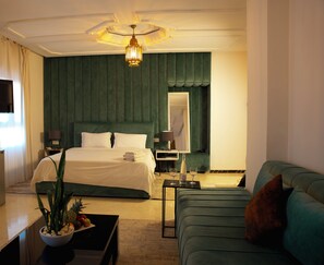 Ein Hotelzimmer mit Bett, einer Couch, einem Fernseher, einer Minibar und einer Pflanze.