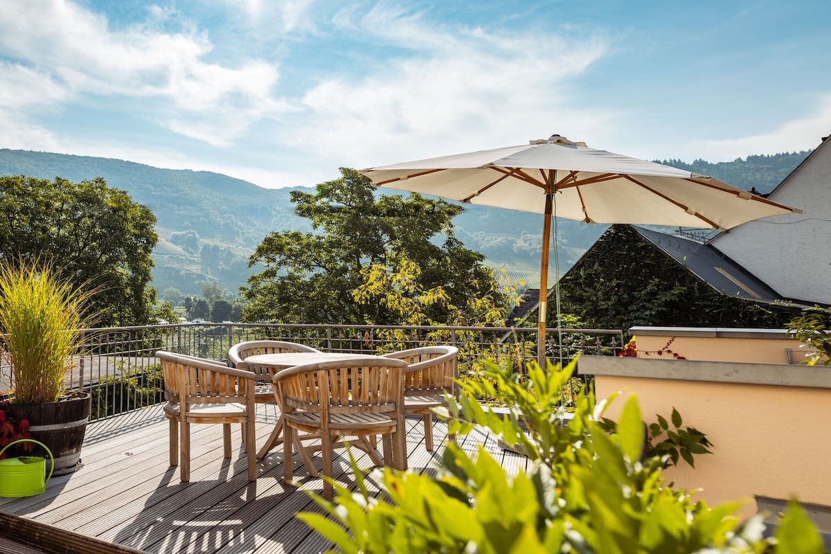 Une terrasse en bois avec une table et des chaises, un grand parasol et une vue sur les montagnes.