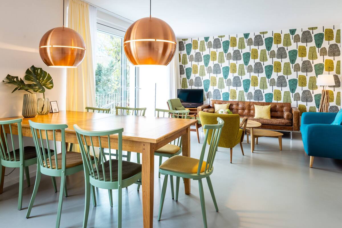 Un salon moderne avec une table à manger en bois, des chaises vertes, un canapé marron et un fauteuil bleu.