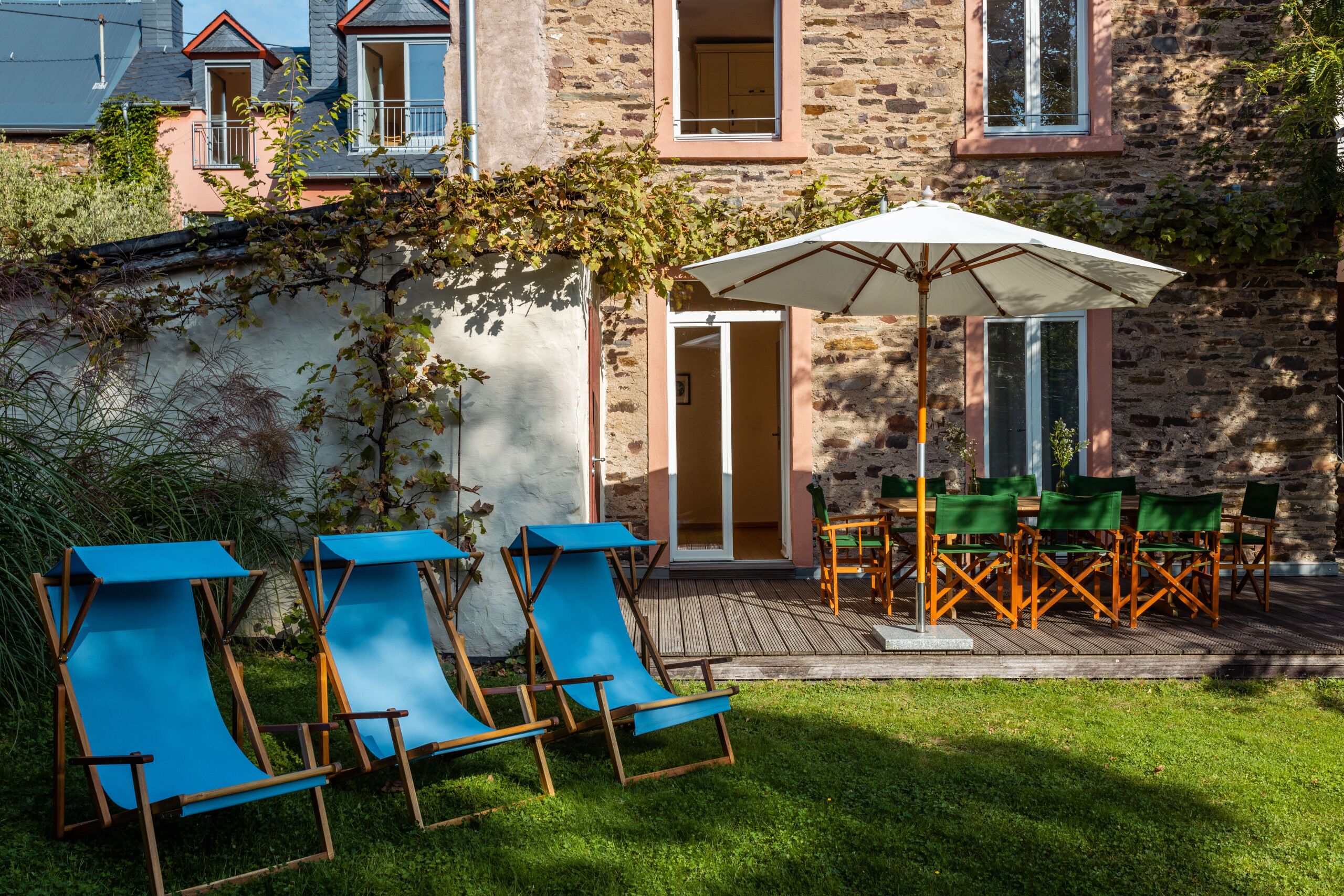 Een stenen gebouw met een houten terras, buiten zitplaatsen en een overdekt gedeelte met een parasol.