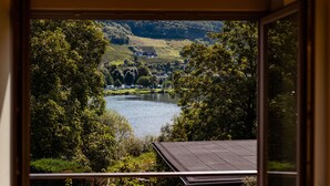 Vista desde un balcón con vistas a un lago, rodeado de abundante vegetación y colinas.