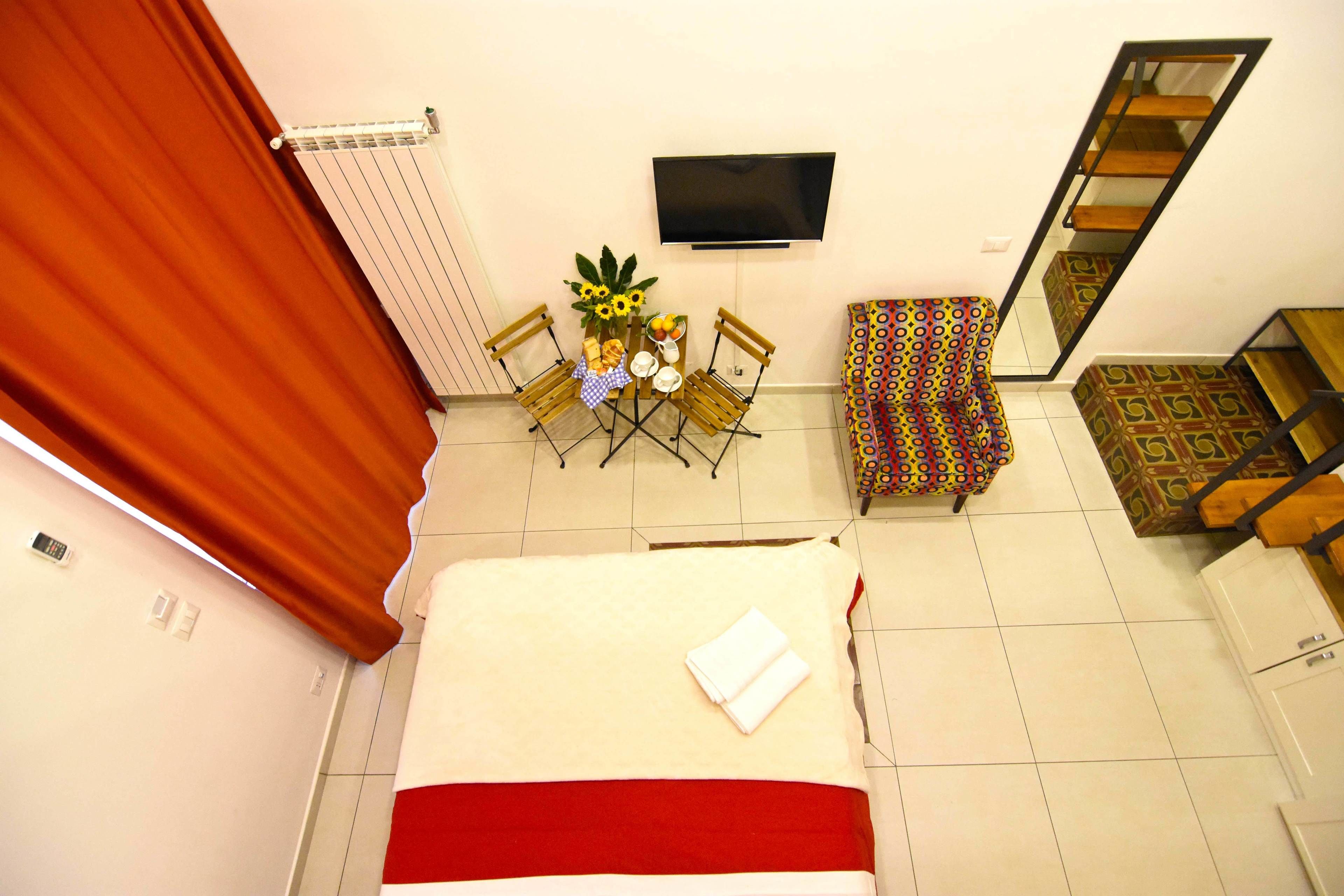 Ein Hotelzimmer mit einem Bett, einem an der Wand befestigten Fernseher, einem kleinen Tisch mit Stühlen und einem gemusterten Sofa.