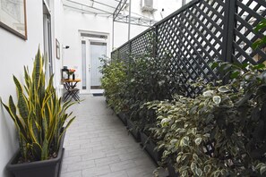 Un couloir étroit, avec des plantes en pot d’un côté et une clôture en treillis noir de l’autre.