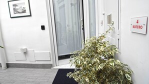 En ren og moderne entré med en dør mærket "4 BOTERO", en lille potteplante og et indrammet billede på væggen.