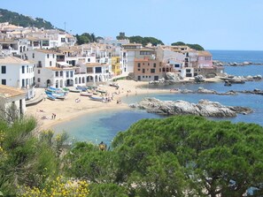 A coastal town with buildings along the beach, boats on the sand, and rocky outcrops in the water. - Apartaments Les Dunes (Pals)