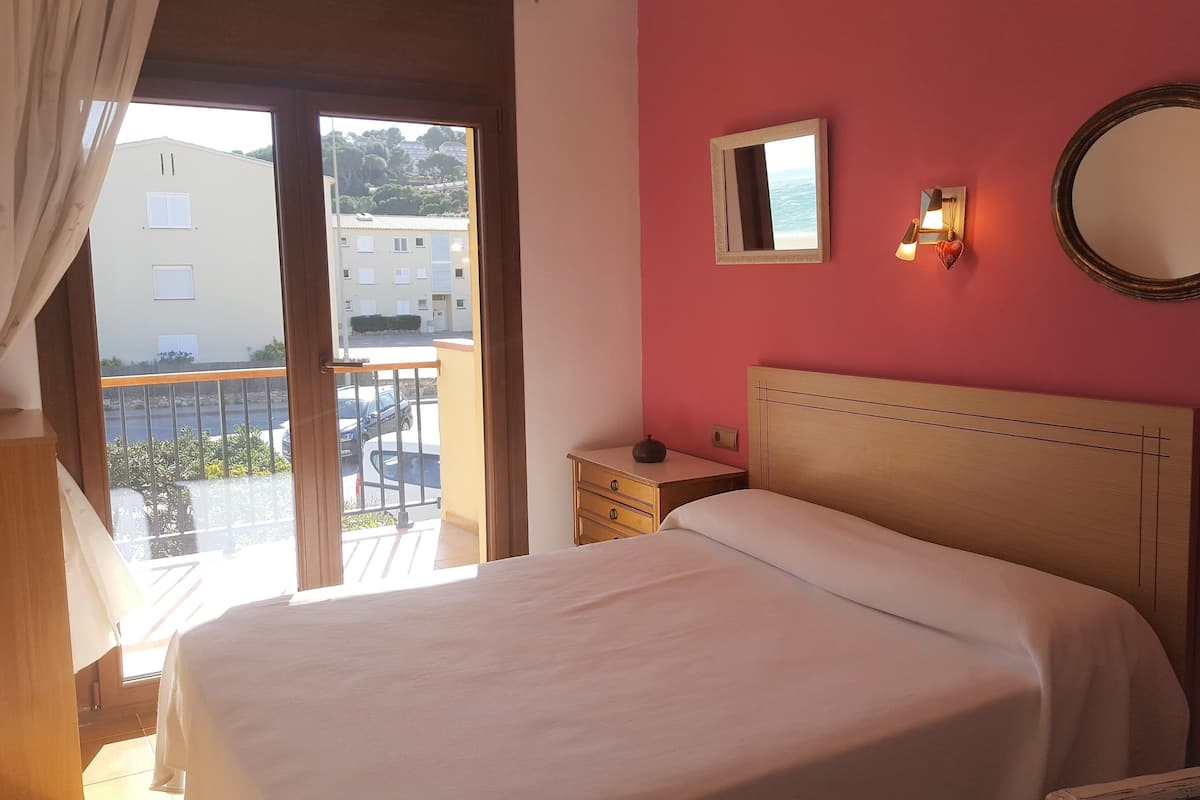 A bedroom with a bed, a nightstand, a mirror, and a view of the outside balcony.