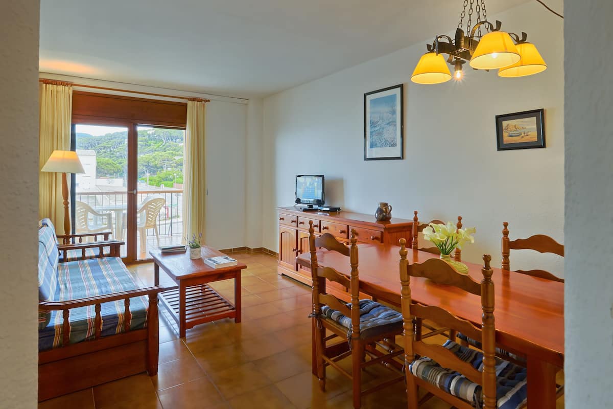 A dining area with a wooden table and chairs, a television, and a balcony with curtains.