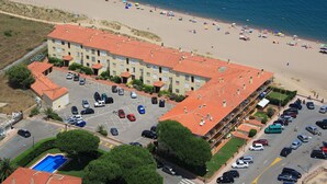 A hotel with a red-tiled roof, a parking lot, and a beach in the background. - Apartaments Les Dunes (Pals)