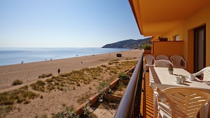 A beach view from a balcony with a table and chairs, overlooking the sandy beach and the sea. - Apartaments Les Dunes (Pals)