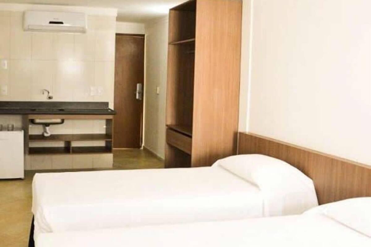 A hotel room with two beds, a kitchenette, and a wooden wardrobe.