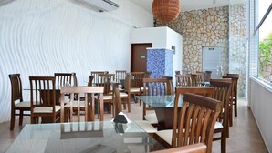 A dining area with wooden chairs and tables, a stone wall, and a blue mosaic feature. - Happy Hotel Ponta Negra (Natal)