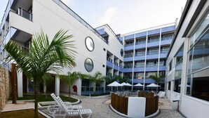 A modern building with multiple floors, outdoor seating area, and palm trees. - Happy Hotel Ponta Negra (Natal)