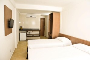 A hotel room with two beds, a small kitchenette, a TV mounted on the wall, and a wooden wardrobe. - Happy Hotel Ponta Negra (Natal)