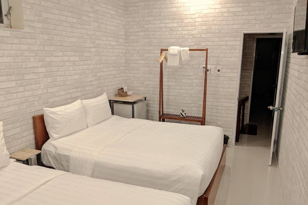 Habitación de hotel con dos camas, cabecero de madera, mesita de noche pequeña y armario con espejo.