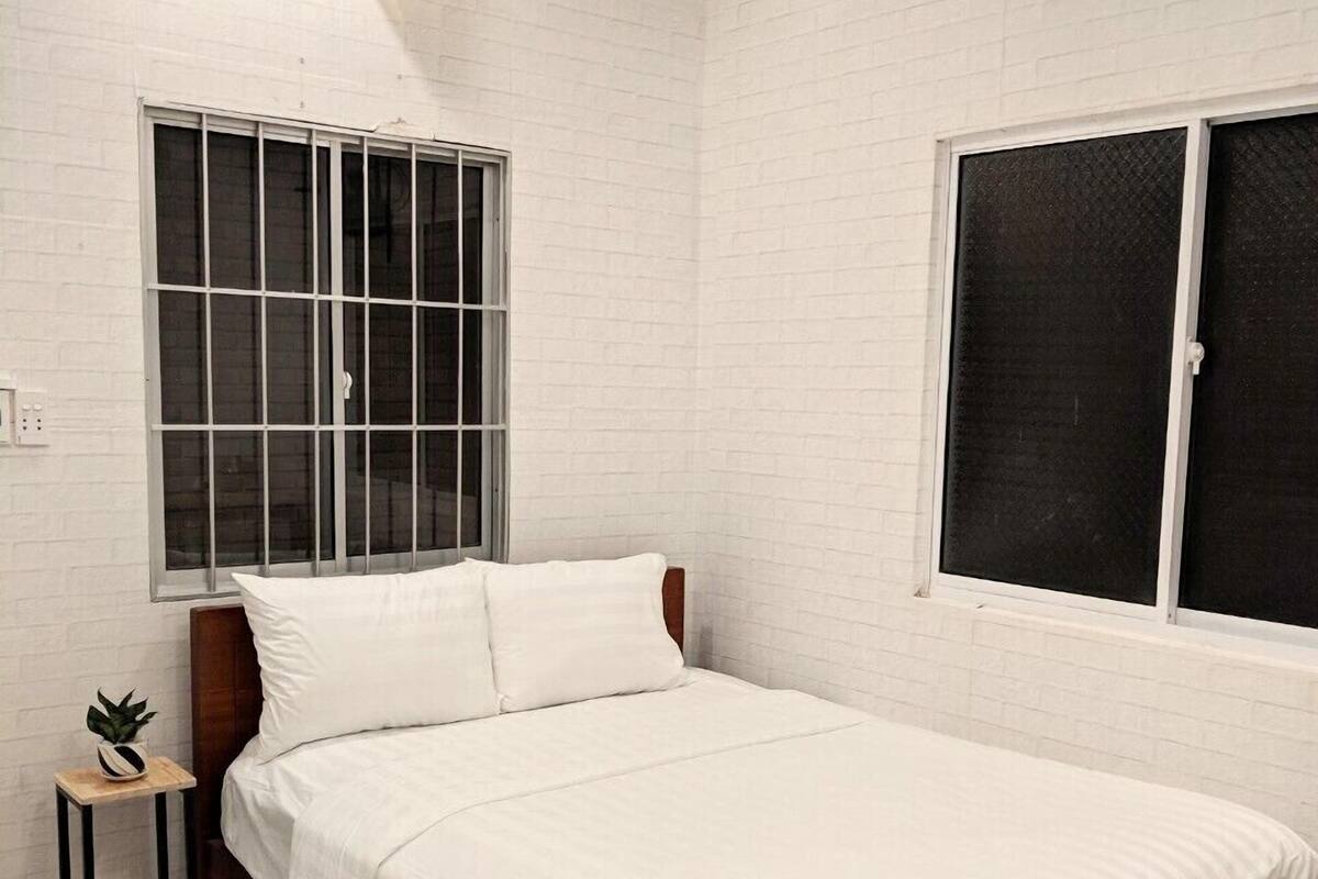 Un dormitorio con cama, ventana, aire acondicionado instalado en la pared y una pequeña mesa con una planta.