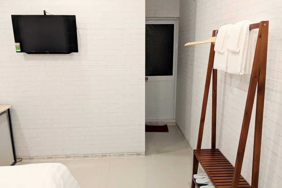 Una habitación de hotel con una cama, un banco de madera con toallas, un televisor de pantalla plana en la pared y una puerta que da a otra habitación.