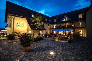 Un patio de hotel con un camino pavimentado, plantas en macetas y mobiliario exterior.