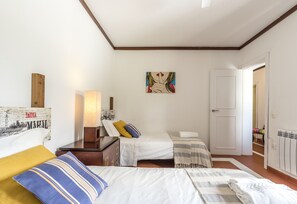 Una camera d'albergo con due letti, una testiera in legno, un quadro, una lampada e una porta che dà su un'altra stanza.