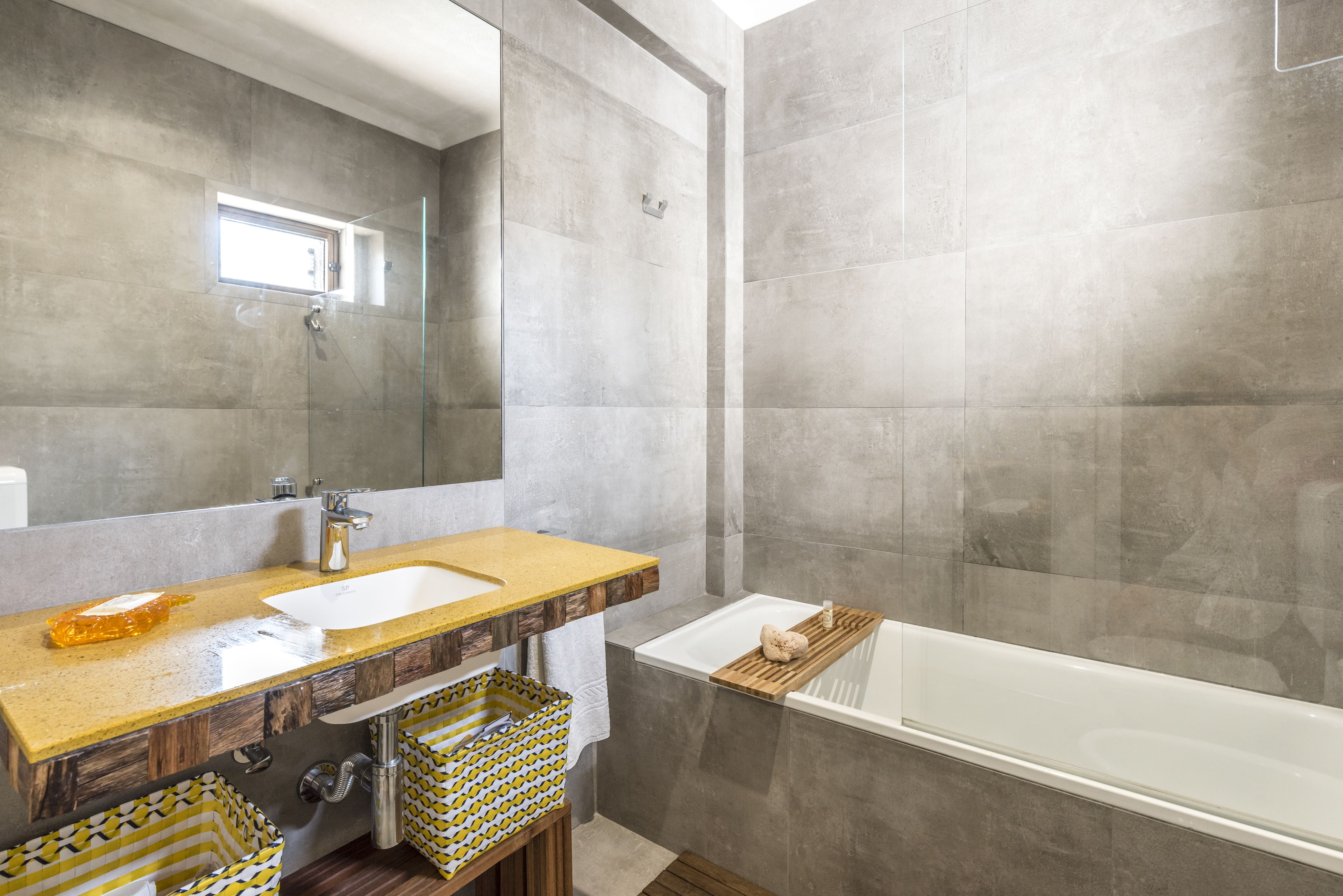A modern bathroom with a large mirror, a wooden vanity, a white sink, and a bathtub.