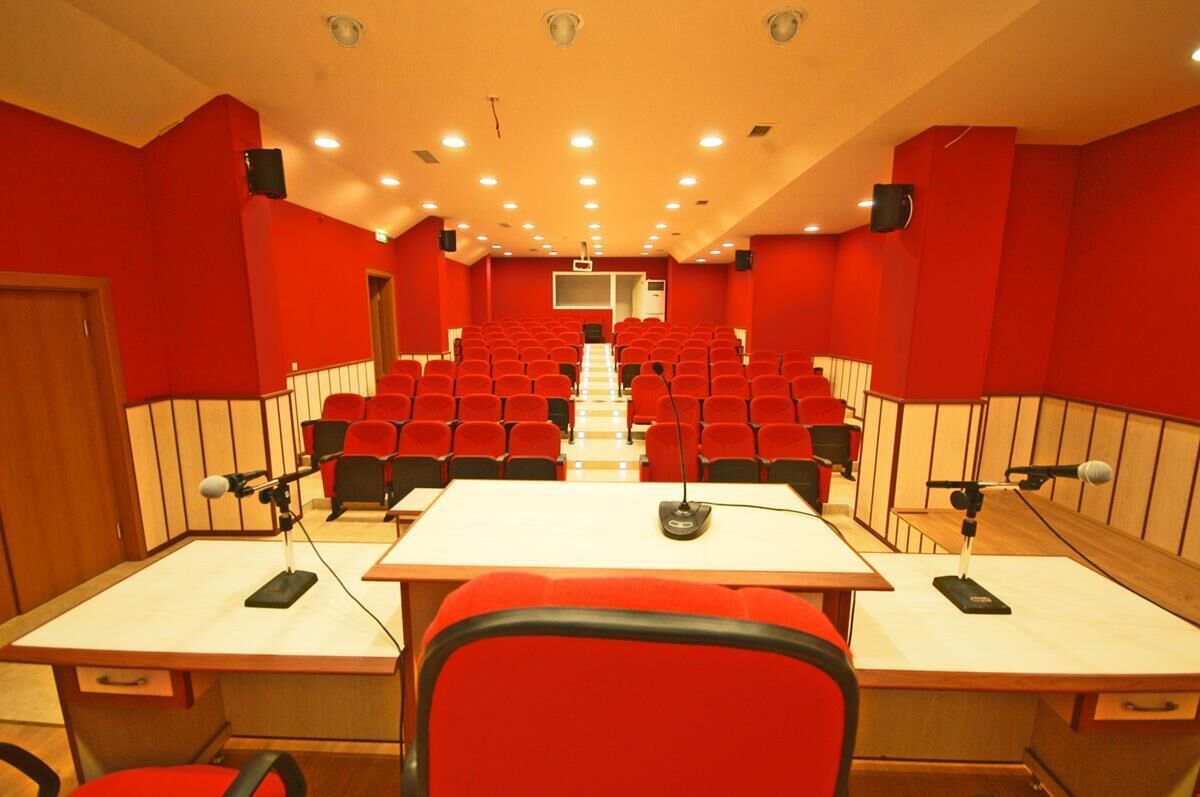 A conference room with red chairs, a long table, and microphones.