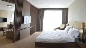 A hotel room with a large bed, a desk, a chair, a TV, and a window with curtains.